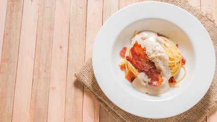 Bacon spaghetti in white plate on wooden background.