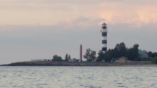 Black and white striped lighthouse at a river mouth during sunset