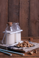 Homemade walnut nut milk in glass bottles with blue straw on a wooden background..