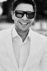 Handsome happy groom in sunglasses and white suit black and whit