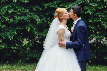 Stylish blonde bride in vintage dress and handsome happy groom holding hands and kissing outdoors