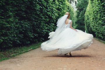 Gorgeous stylish blonde bride in vintage white dress walking in the park
