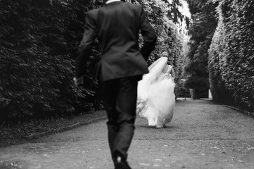Gorgeous stylish blonde bride in vintage white dress and elegant groom walking in the park