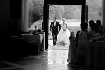 Black and white happy elegant bride and stylish groom entering wedding venue