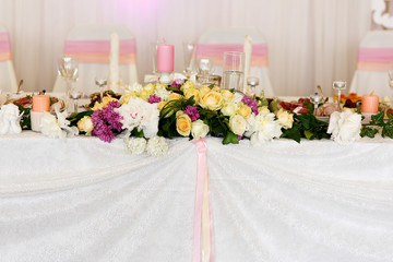 Traditional white wedding table with flowers candles and wine bottles on top and a curtain in the background