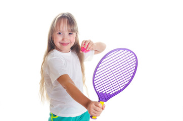 The little girl holds in hand a tennis racket with a ball and smiles