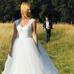 Happy handsome groom running towards beautiful elegant bride in the field