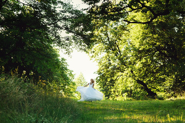 Beautiful romantic blonde bride in white dress dancing in the forest