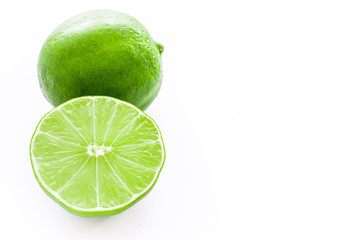 Close up photo of one cut-in-half slice of lime, with one whole lime behind. The background is isolated.
