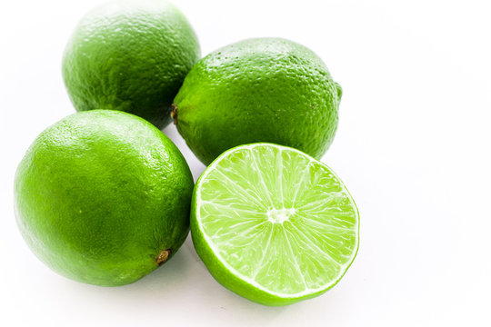Close up photo of one cut-in-half slice of lime, with three whole lime behind. The background is isolated.