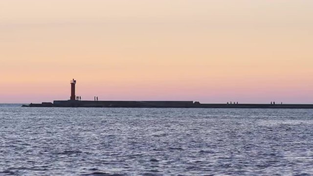 People hanging out at the tip of a breakwater during a summer evening