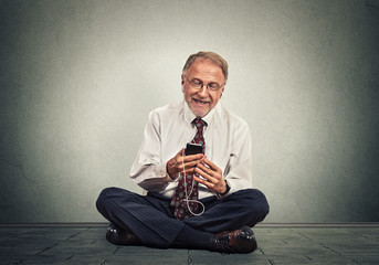 senior executive man sitting on a floor using smart phone texting listening music