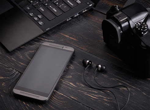 Laptop, smart phone, photo camera and headset on wooden background