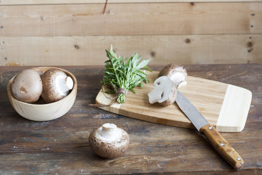 Champignon mushrooms, a knife, bagging and herbs on a wooden board on wooden background