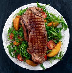 rare beef steak with roasted potatoes, tomatoes and wild rocket leaves. on old blue stone background