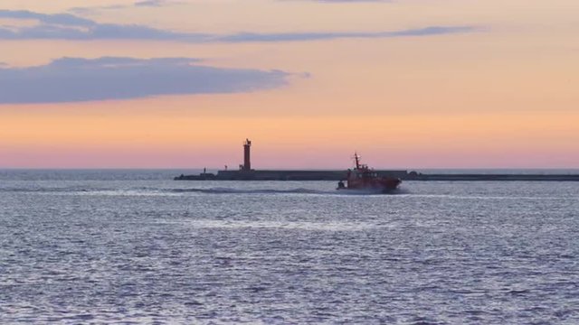 Pilot ship returning to port during vivid summer sunset, breakwater in background