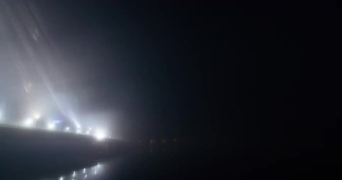 Time lapse of a panning reveal shot of Riga suspension bridge wrapped in a thick fast moving fog with busy evening traffic