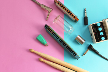 Music concept - guitar pedals, drum sticks, harmonica, audio plug, guitar slide and guitar picks on half blue half pink background