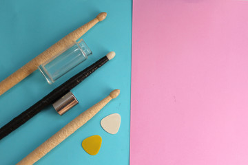 Drum sticks, guitar picks and guitar slide on half blue half pink background