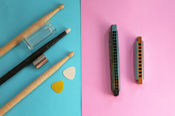 Drum sticks, guitar picks and guitar slide on blue background and harmonica on pink background