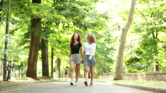 Two beautiful girls walking holding hands at park

