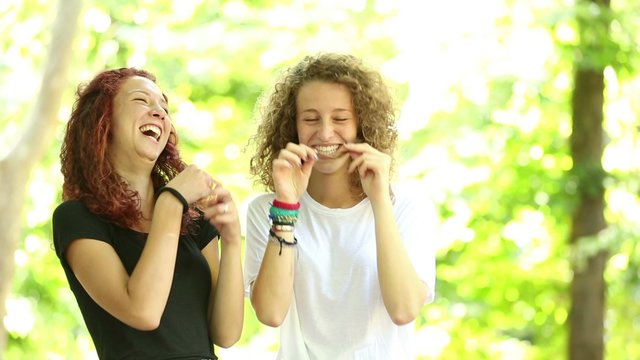 Two girls playing at park and making moustache with their hair
