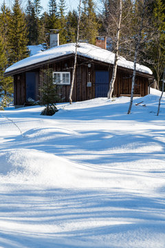 Typical black Norwegian cabin surrounded by snow in the forest