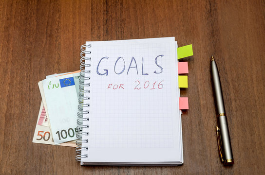 Notebook with text goals of year 2016 with dollar on wooden