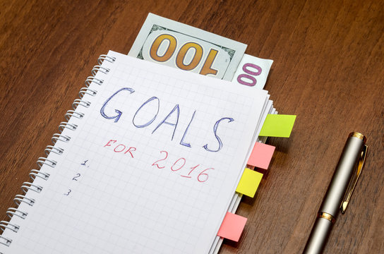 Notebook with text goals of year 2016 with dollar on wooden