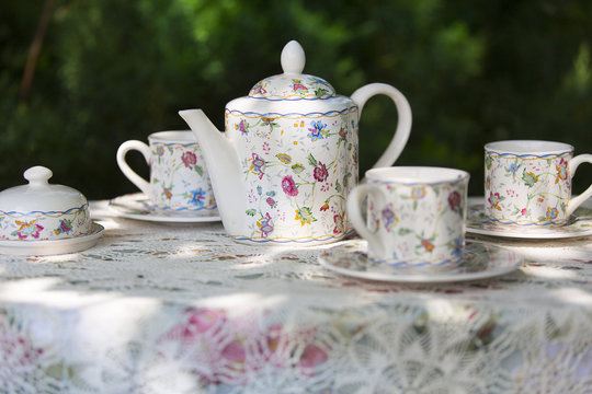Белый чайный сервиз в цветочек на столе с кружевной скатертью 
