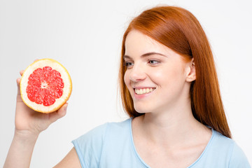 Smiling young happy redhead female looking on half of grapefruit
