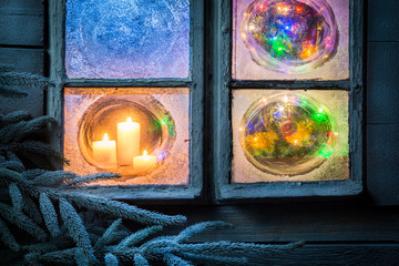 Beautiful burning candles for Christmas in frozen window at eve