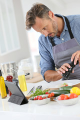 Man in kitchen cooking dish and using digital tablet