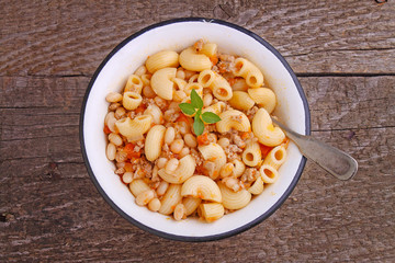 pasta with meat and beans in a white bowl on the old wooden background