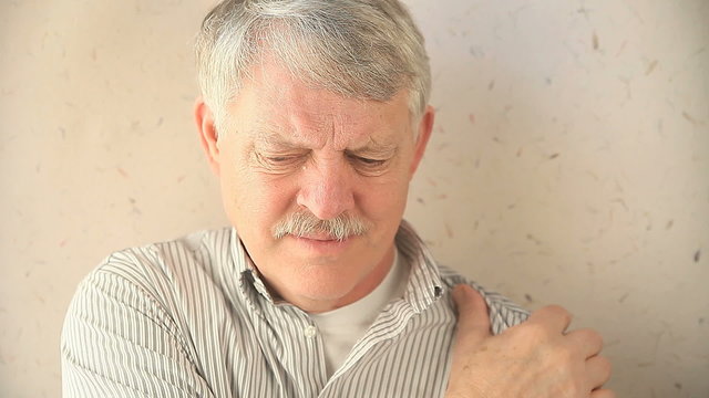 An older man massages his painful shoulder.
