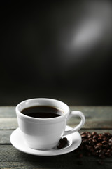 Cup of coffee and coffee grains on wooden table, on gray background
