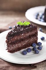 Chocolate cake with chocolate cream and fresh blueberries on plate, on wooden background
