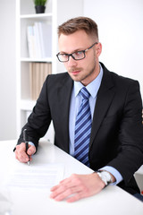 Portrait of young business man sitting at the desk on office background.