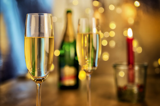 Image of two champagne glasses with bottle, candle and blur lights in background