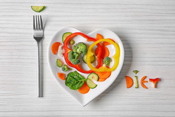 Useful cut vegetables on a plate in the form of heart on wooden table top view