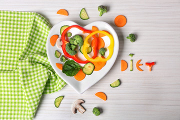 Useful cut vegetables on a plate in the form of heart on wooden table top view