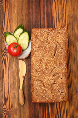 
Ржаной домашний хлеб с кунжутом рядом с блюдцем с кусочками огурца и помидором и деревянным ножом на деревянном столе
