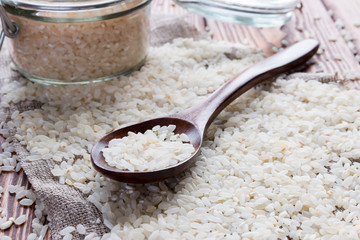 Bank with rice and wooden spoon on a background of spilled rice