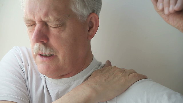 A senior man winces in pain when he tries to move his shoulder.