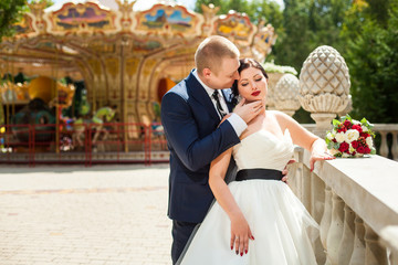 Bridegroom hugging bride near carousel