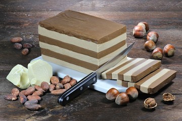 Block Schichtnougat mit Haselnüssen, Kakaobohnen und Kakaobutter auf Holzhintergrund