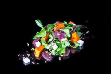Salad of pumpkin, corn leaves, feta and sunflower seeds on a black background