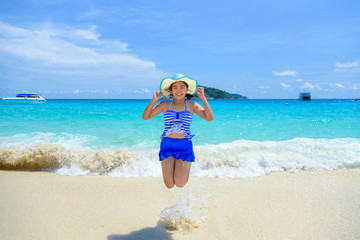 Fototapeta na wymiar Tourist woman in a blue white striped swimsuit jumping with happy on the beautiful beach sea and sky during summer at Koh Miang Island, Mu Ko Similan National Park, Phang Nga, Thailand