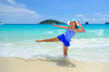 Fototapeta na wymiar Beautiful woman in a blue white striped swimsuit standing with gestures have fun and happy under summer sky on the beach of Koh Miang Island in Mu Ko Similan National Park, Phang Nga, Thailand