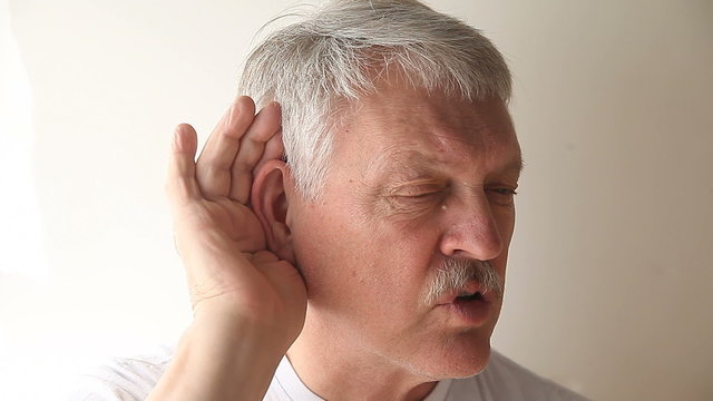 An older man strains to hear what someone is saying.